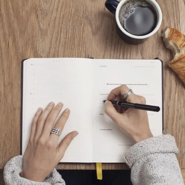 Hands writing in a notebook beside a coffee